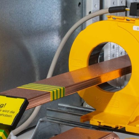 Eine Kupferschiene geht durch einen runden gelben Stromwandler